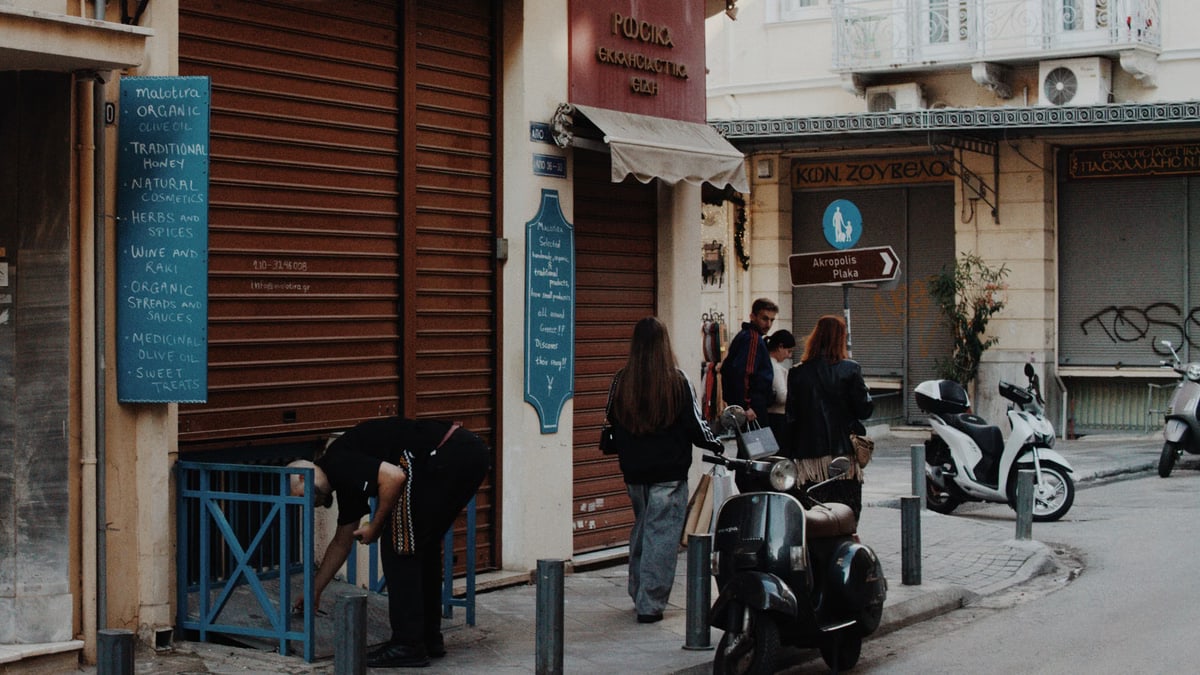 A lively Athens street captures pedestrians, scooters, and shops in the evening light.